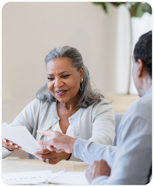 An older woman reviews documents with a lawyer at a table in a well lit room.